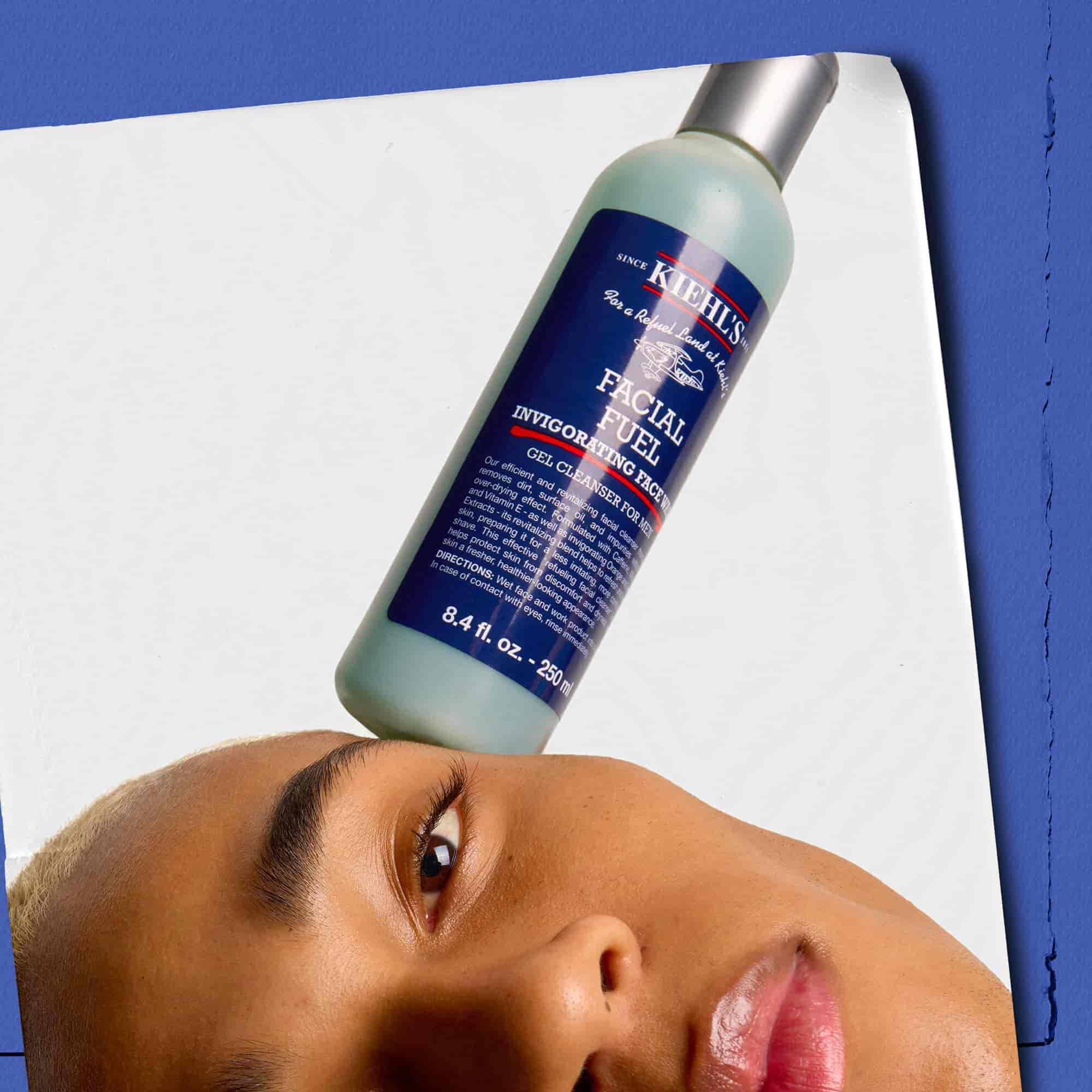 Модел с бутилка енергизиращ измиващ гел Kiehl's Facial Fuel, балансирана върху лицето му