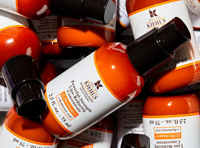 Флакони с оранжев серум от Kiehl's, разположени хаотично върху бял фон.