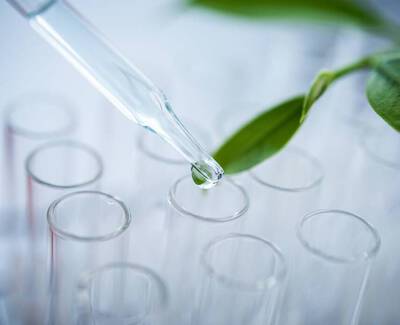 A dropper releasing a drop of liquid above several test tubes, with a green leaf in the background.