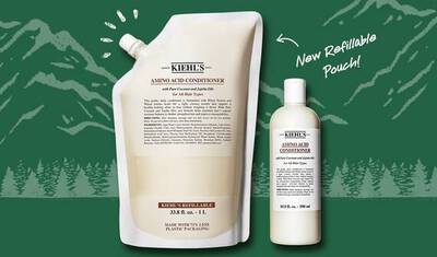 Image showing a refillable pouch of Kiehl's Amino Acid Conditioner alongside a standard bottle of the same product, set against a forest background. The pouch is labeled "New Refillable Pouch!"