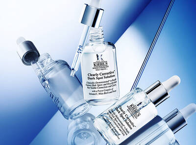 Серум за корекция на тъмни петна Kiehl's на син фон, с фокус върху бутилки и капкомер.