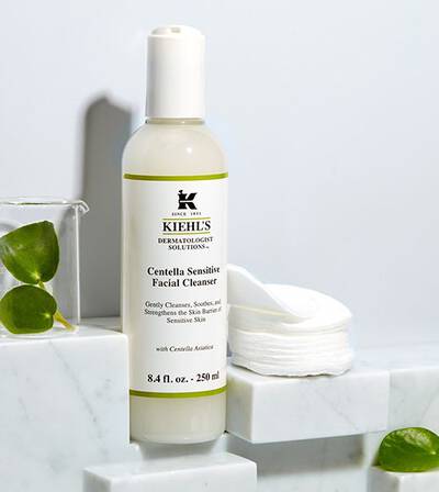 Флакон с почистващ гел за лице Kiehl's Centella Sensitive на мраморна повърхност с памучни дискове в близост.