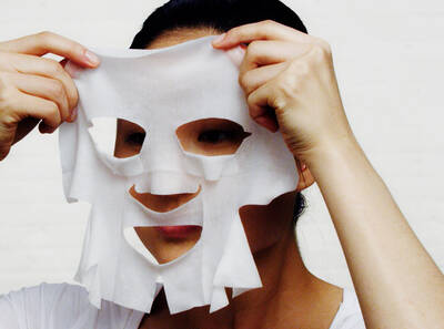 Жена поставя лицева маска от хартия на лицето си, подготовка за грижа за кожата.