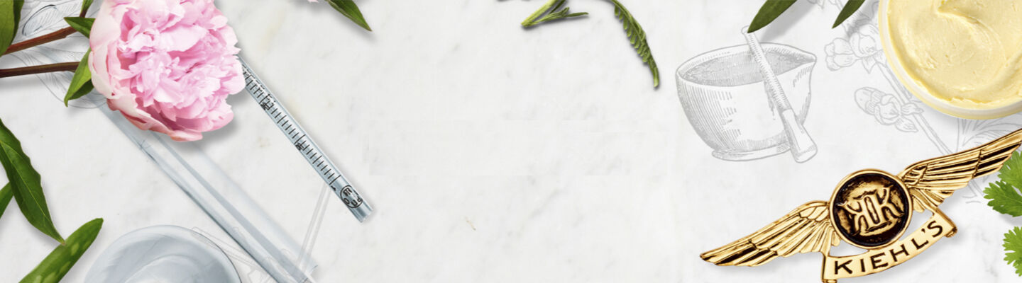 A flat lay arrangement featuring botanical elements, glass laboratory tools, and a Kiehl's brand emblem, set against a marble background.
