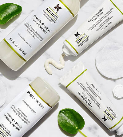 A collection of Kiehl's skincare products, including a facial cleanser and cream, displayed with green leaves and cotton pads.