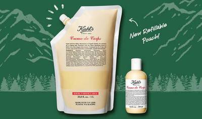 An image featuring Kiehl's Creme de Corps moisturizer displayed in both a refillable pouch and a smaller bottle, set against a green background with mountain outlines. Text highlights the new refillable pouch design for reduced plastic use.