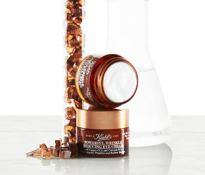 Kiehl's Powerful Wrinkle Reducing Eye Cream jar with a glass flask and shimmering copper crystals in the background.