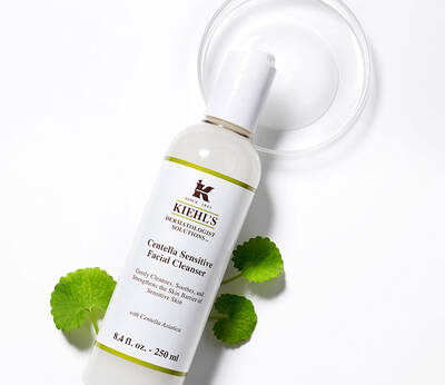 A bottle of Kiehl's Centella Sensitive Facial Cleanser, with a clear pump and green leaves nearby, on a white background.
