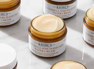 Крем с екстракт от невен и серум в стъклени бурканчета на Kiehl's, разположени на мраморна повърхност.