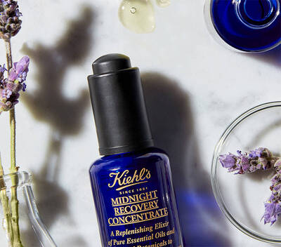 Серум за възстановяване на кожата Kiehl's, поставен на мраморна повърхност, с лавандула и капки масло около него.