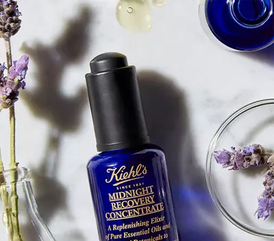 Серум за възстановяване на кожата Kiehl's, поставен на мраморна повърхност, с лавандула и капки масло около него.
