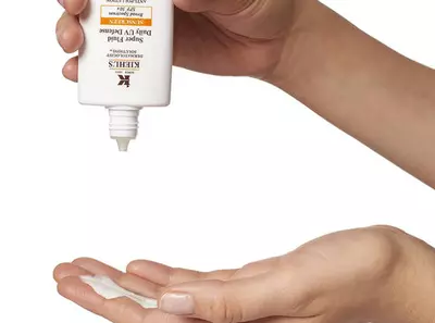 Ръка изсипва крем от туба с етикет на Kiehl's върху друга ръка. Козметичен продукт за ежедневна употреба.
