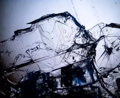 Close-up of intricate, fragmented pieces of transparent crystal with distinct lines and textures, illuminated against a light background.