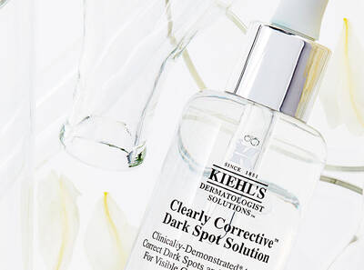 Флакон с серум за коригиране на тъмни петна от Kiehl's, разположен върху светъл фон с цветя.